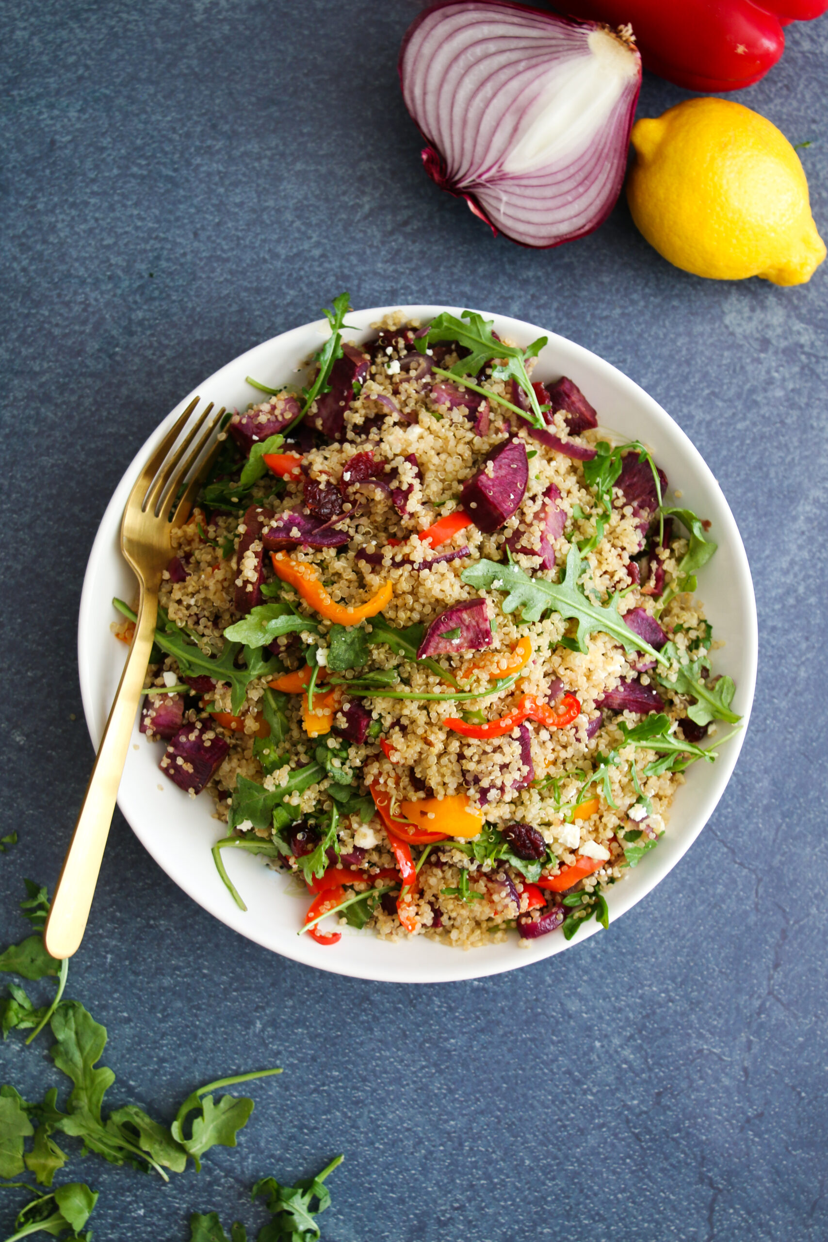 Roasted veggie quinoa salad in a white bowl, on a speckled navy blue background.