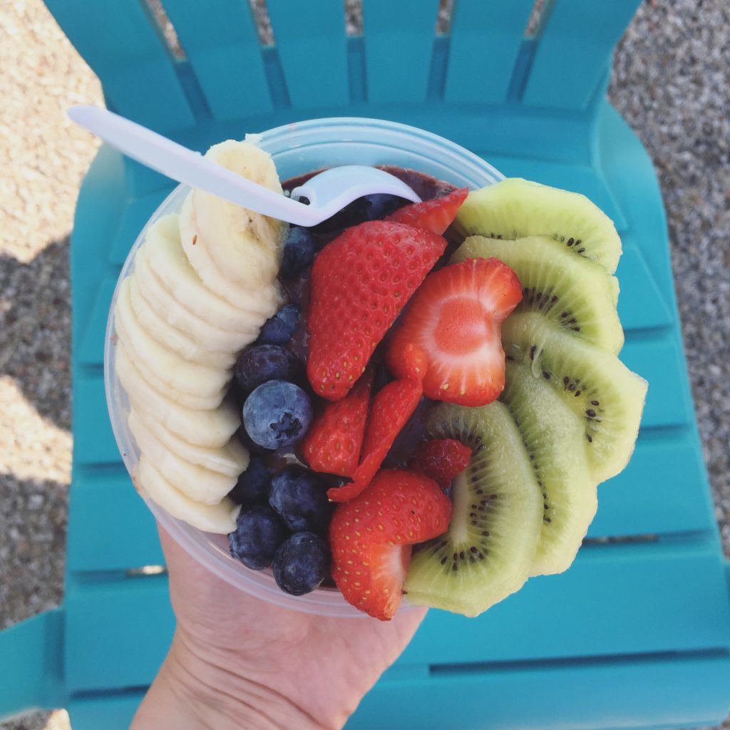 Acai bowl topped with berries, kiwi, and banana on a teal background.