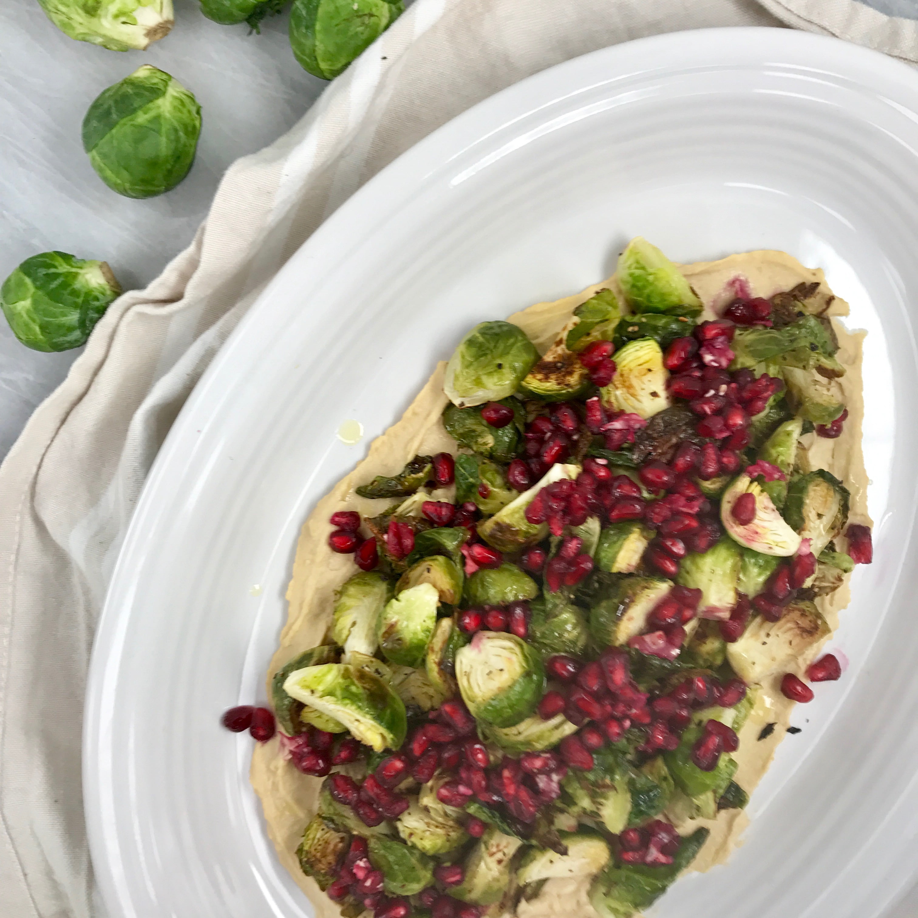 Crispy Brussels with pomegranate and hummus on a white plate, on a marble background.