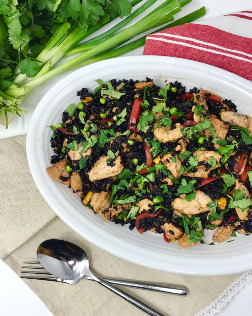 Thai fried rice made with forbidden rice, on a white plate, with spring onions, and cilantro in the background.