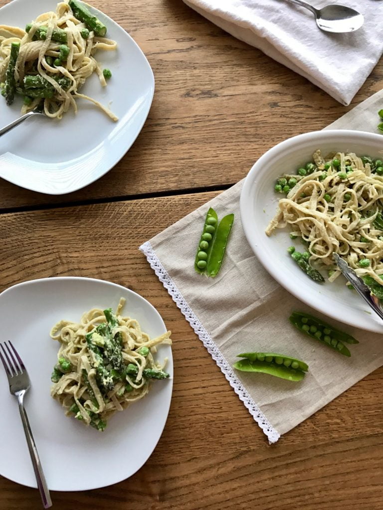 Creamy lemon pasta with peas and asparagus, on three white plates, on a wooden background.