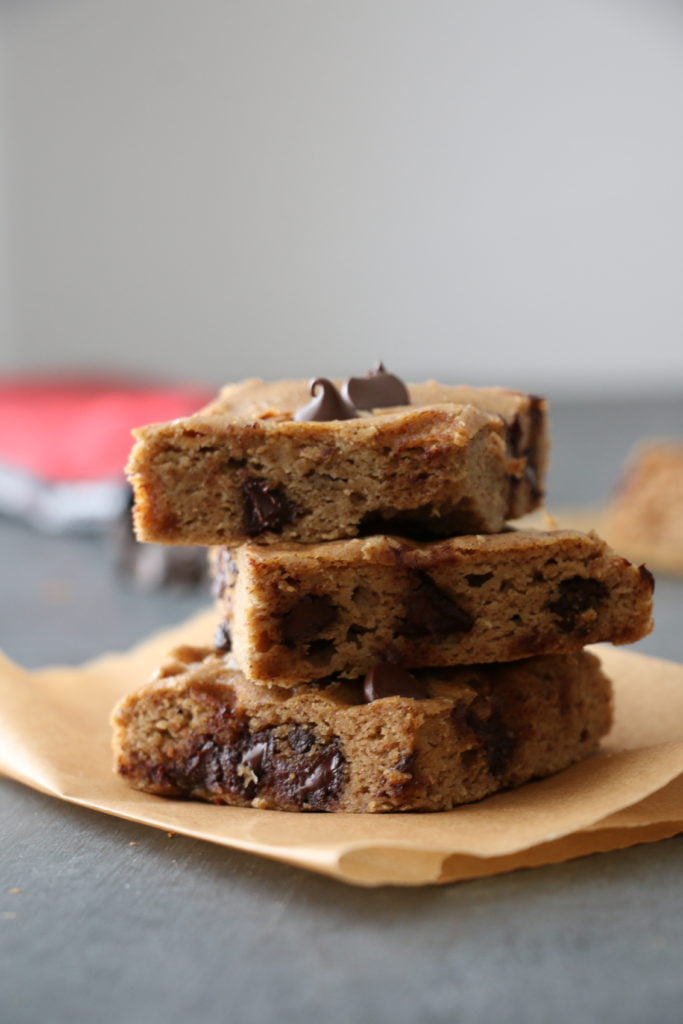 Stack of three chickpea blondie squares on parchment paper, on a black background. 