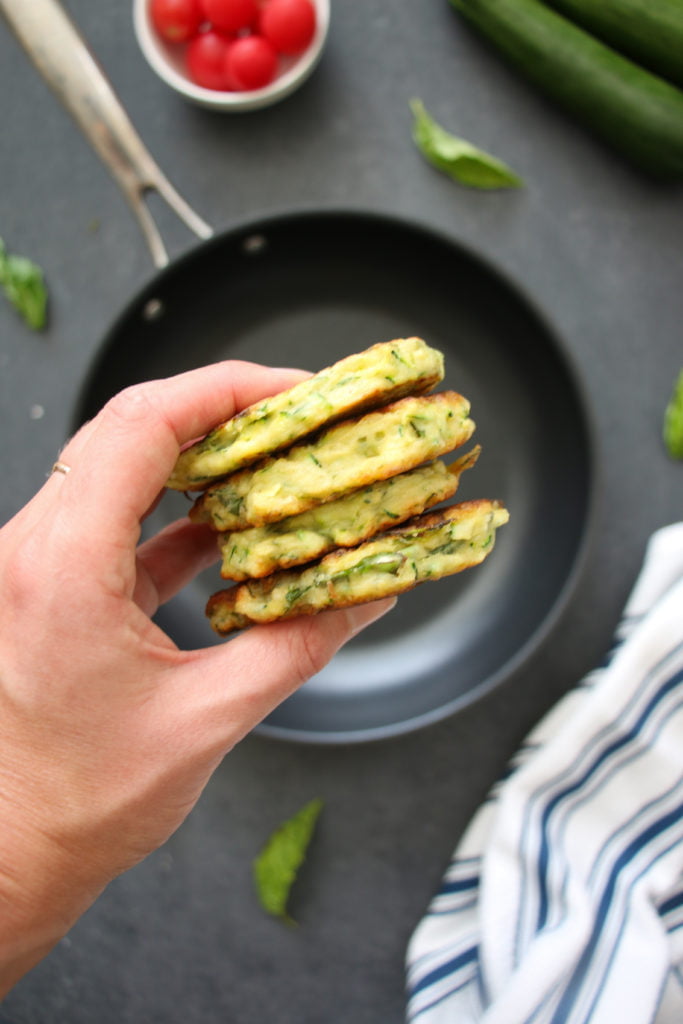 Stack of four zucchini fritters on a black background.