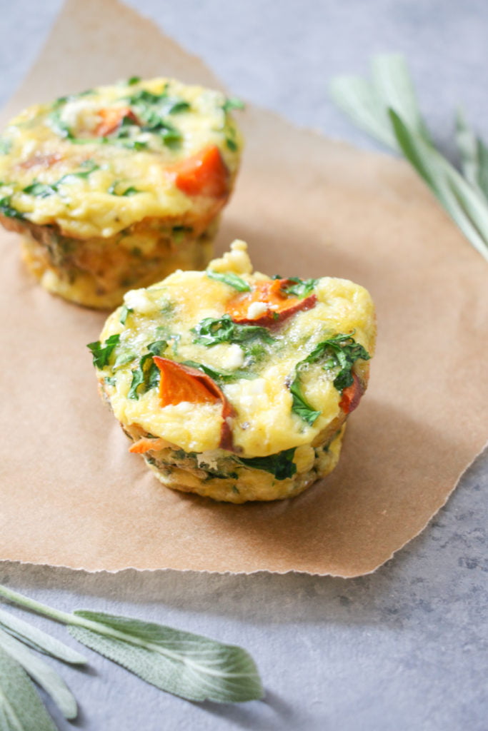 Two sweet potato and sage egg muffins on parchment paper on a gray background