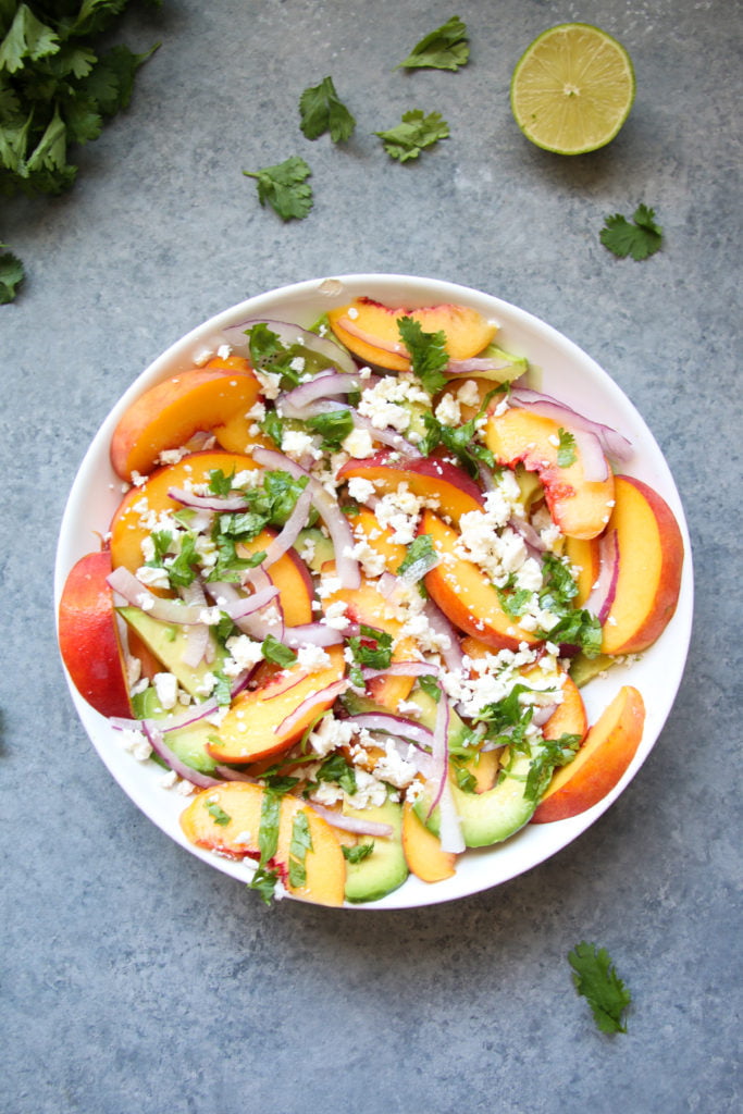 Peach, avocado and feta salad in a white bowl, on a gray background.