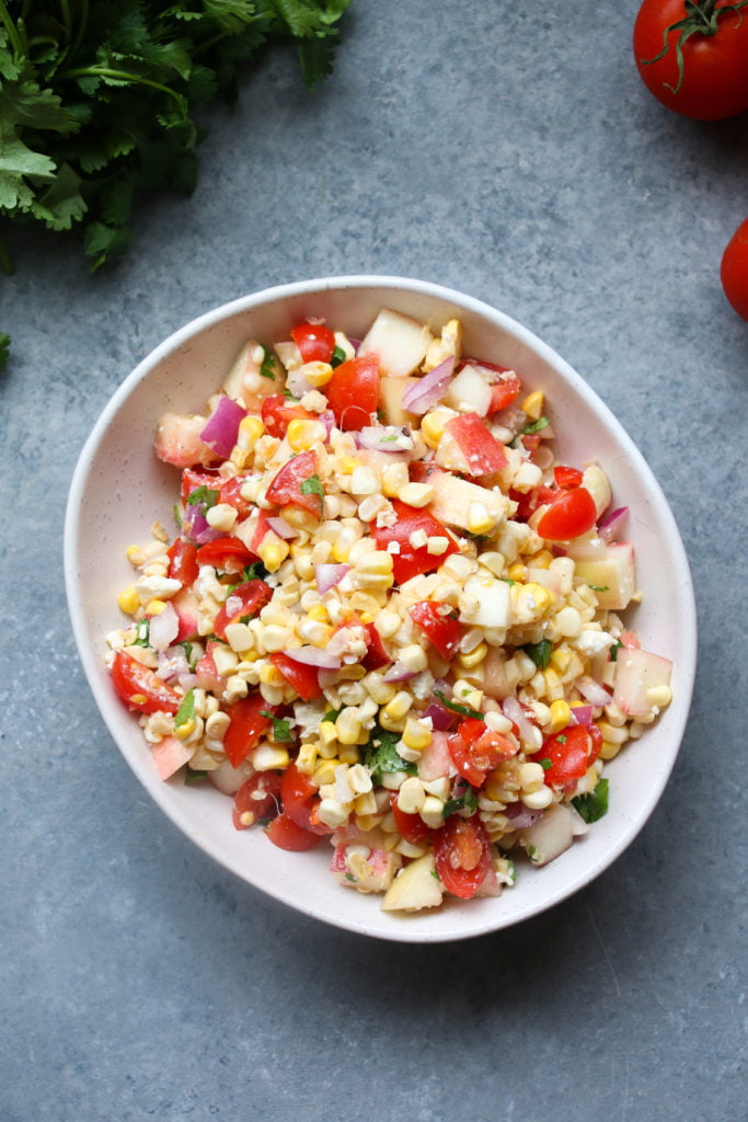 Summer corn salad with stone fruit and feta, in an off-white bowl, on a gray background.