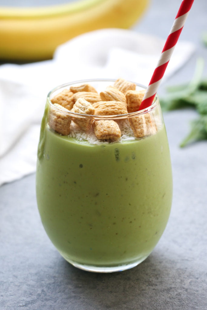 Tropical turmeric green smoothie in a clear glass with a red and white straw, on a gray background.