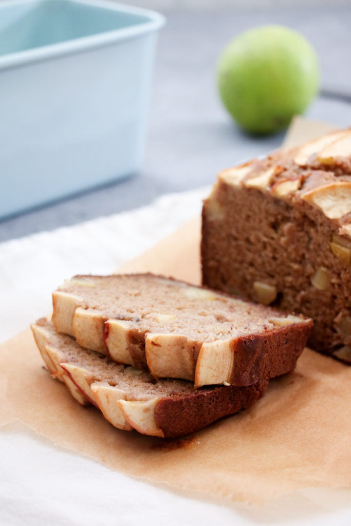 Two slices of GF apple and cinnamon banana bread stacked on top of each other on parchment paper, with a green apple in the background.