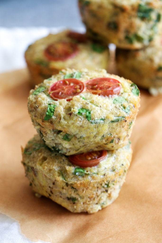 Two spinach and quinoa muffins stacked on top of each other on parchment paper.