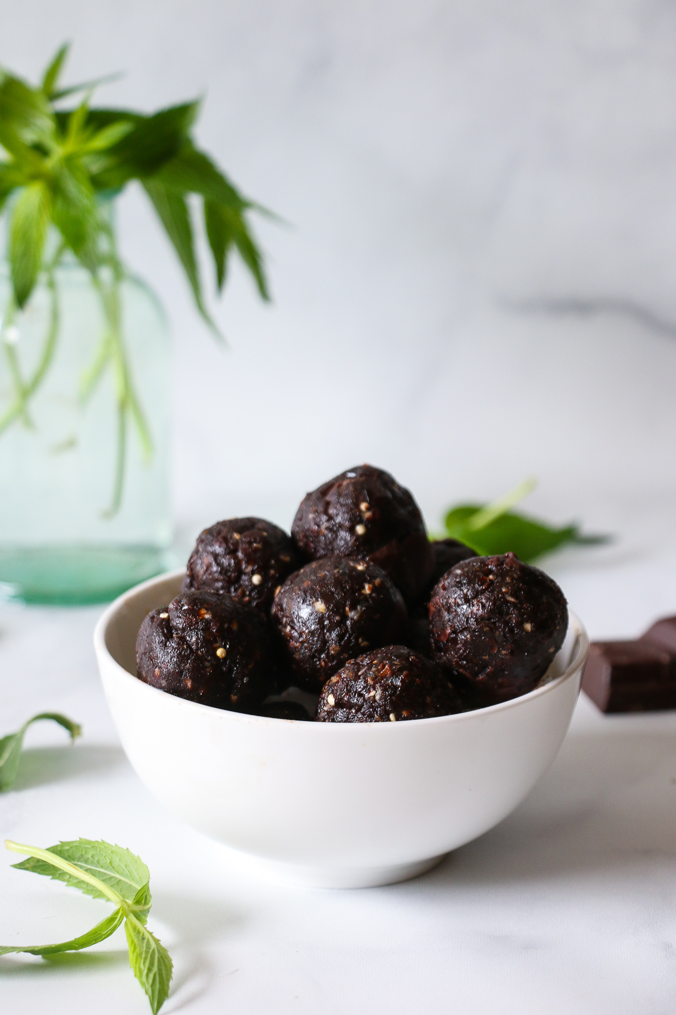 Healthy chocolate-mint truffles, made with dates, and tahini, in a white bowl, on a marble background.