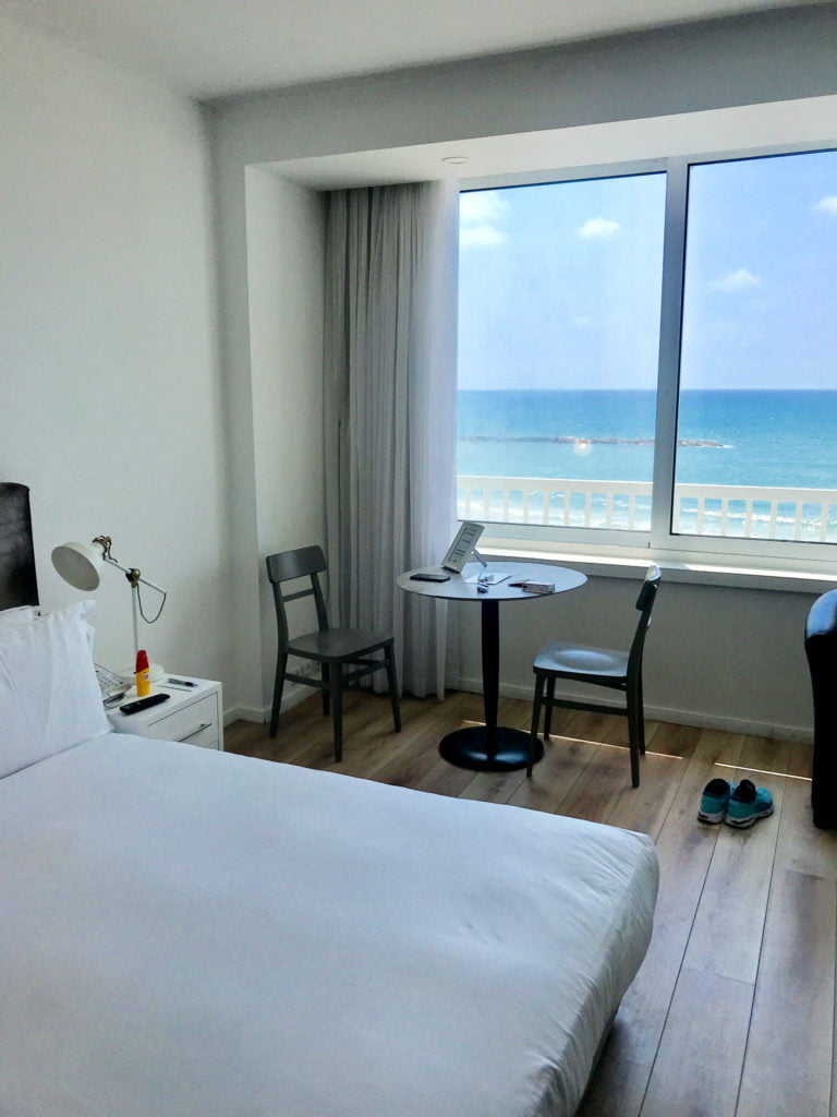 View from our studio at Sea Executive Suites, Tel Aviv: White bed in the foreground, beach in the background. 