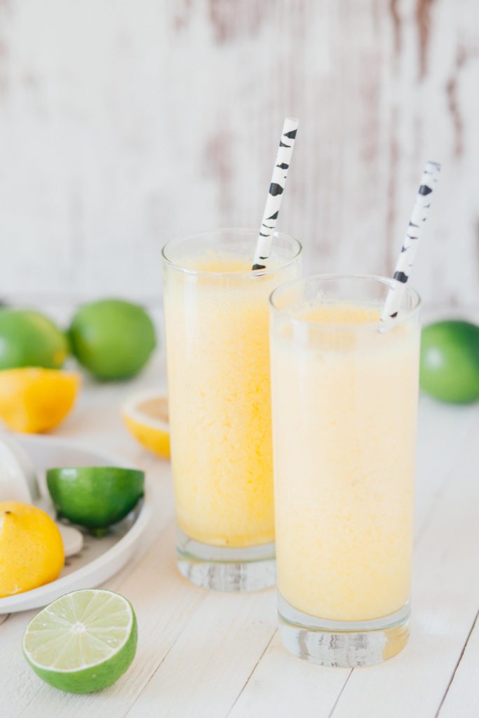 2019 food trend: Functional beverages. Yellow citrus smoothies on a white background, surrounded by lemons and limes. 
