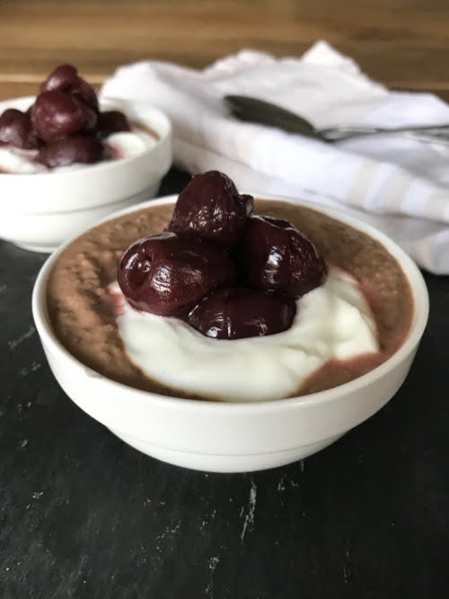 Chocolate-cherry chia pudding side-on in a white bowl, on a black background. 