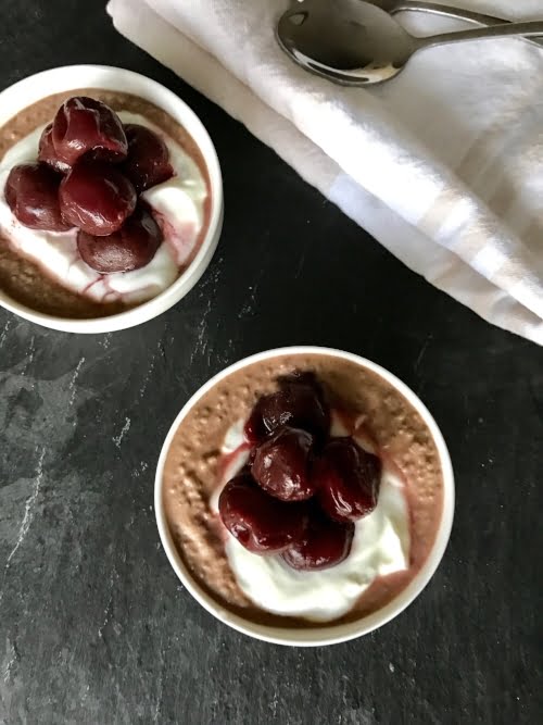 Two chocolate-cherry chia pudding parfait in small white bowls on a black background. 