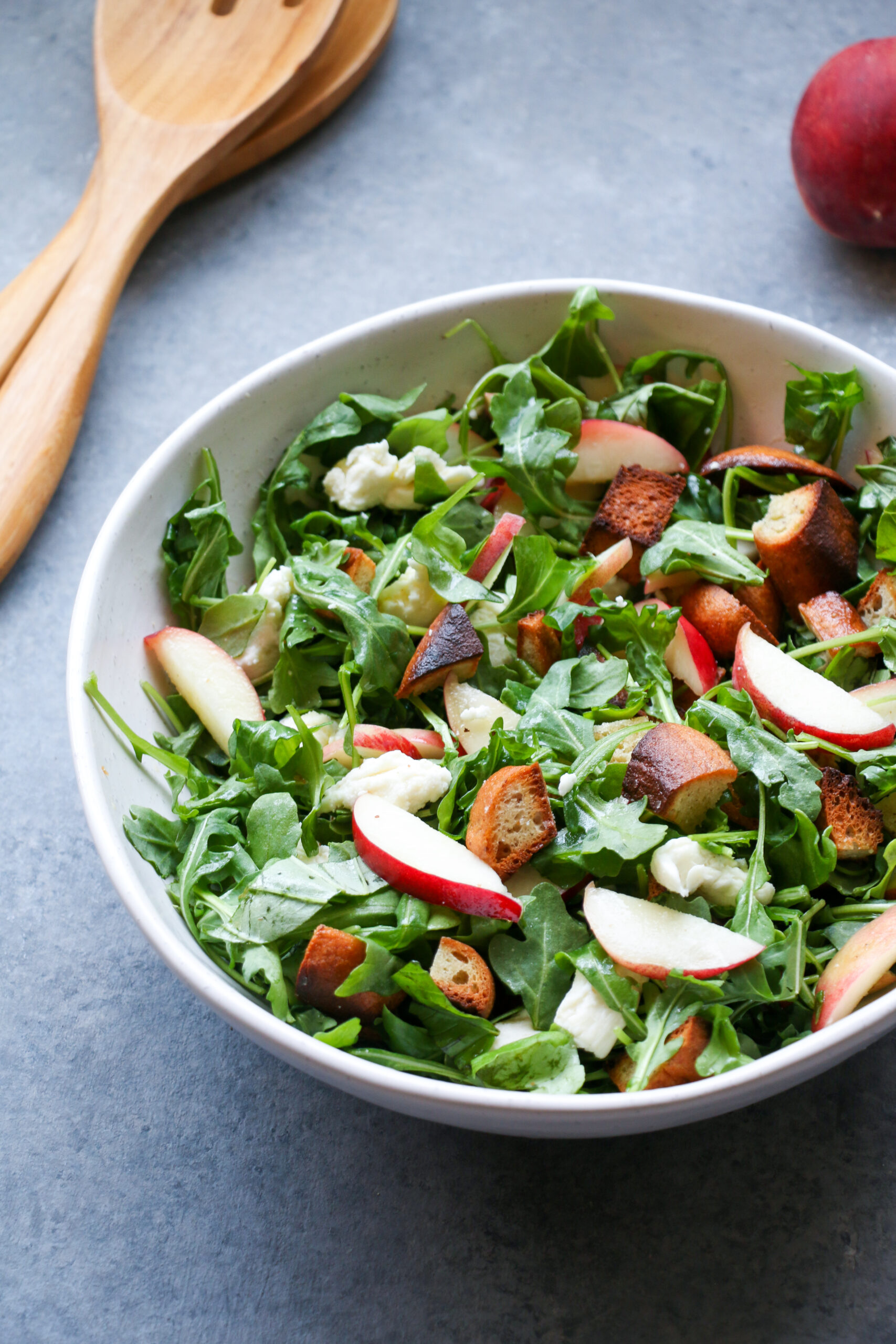 Peach Caprese panzanella salad in a white bowl on a gray background
