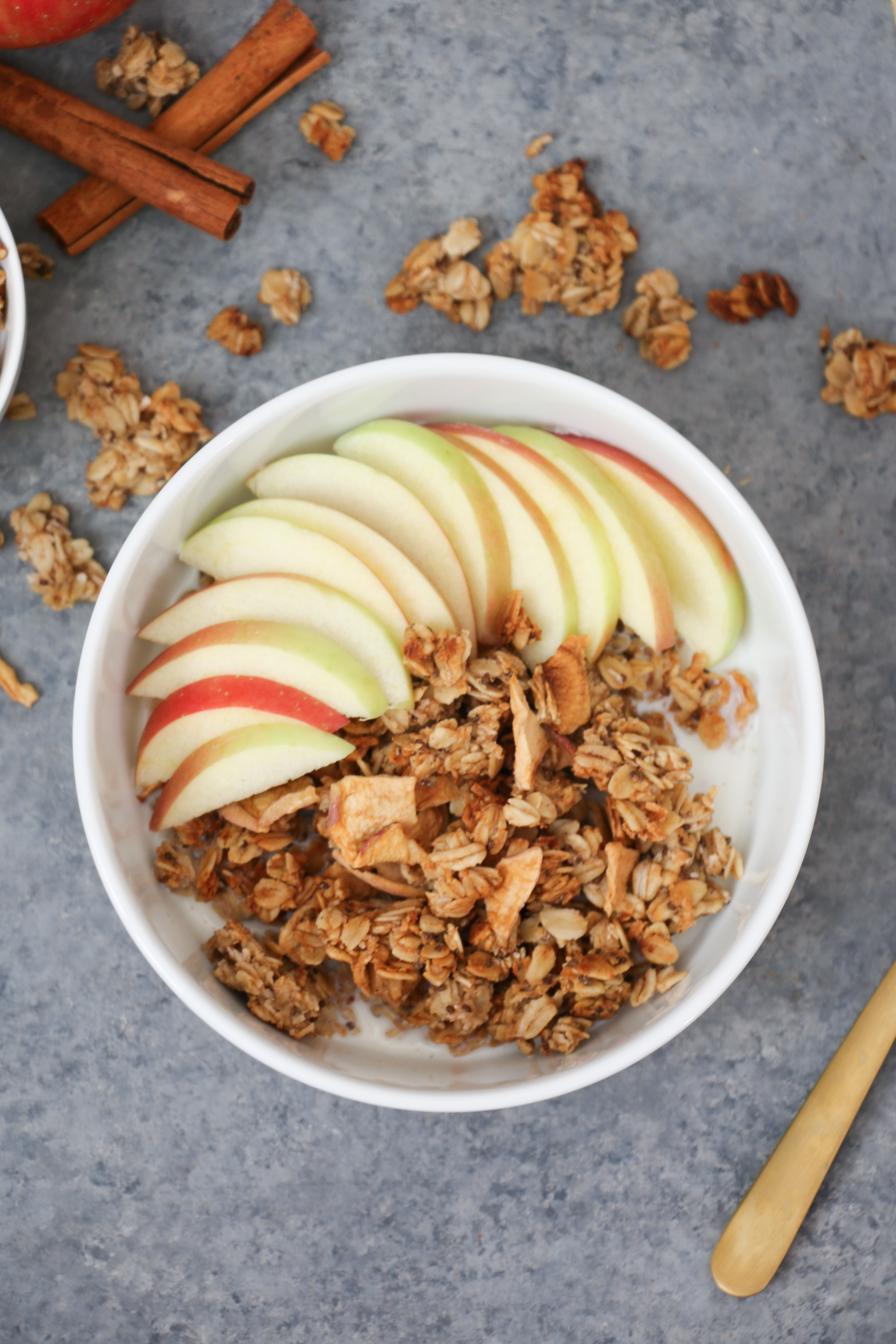 Overhead shot of apple and cinnamon granola topped with apples on a gray background. 