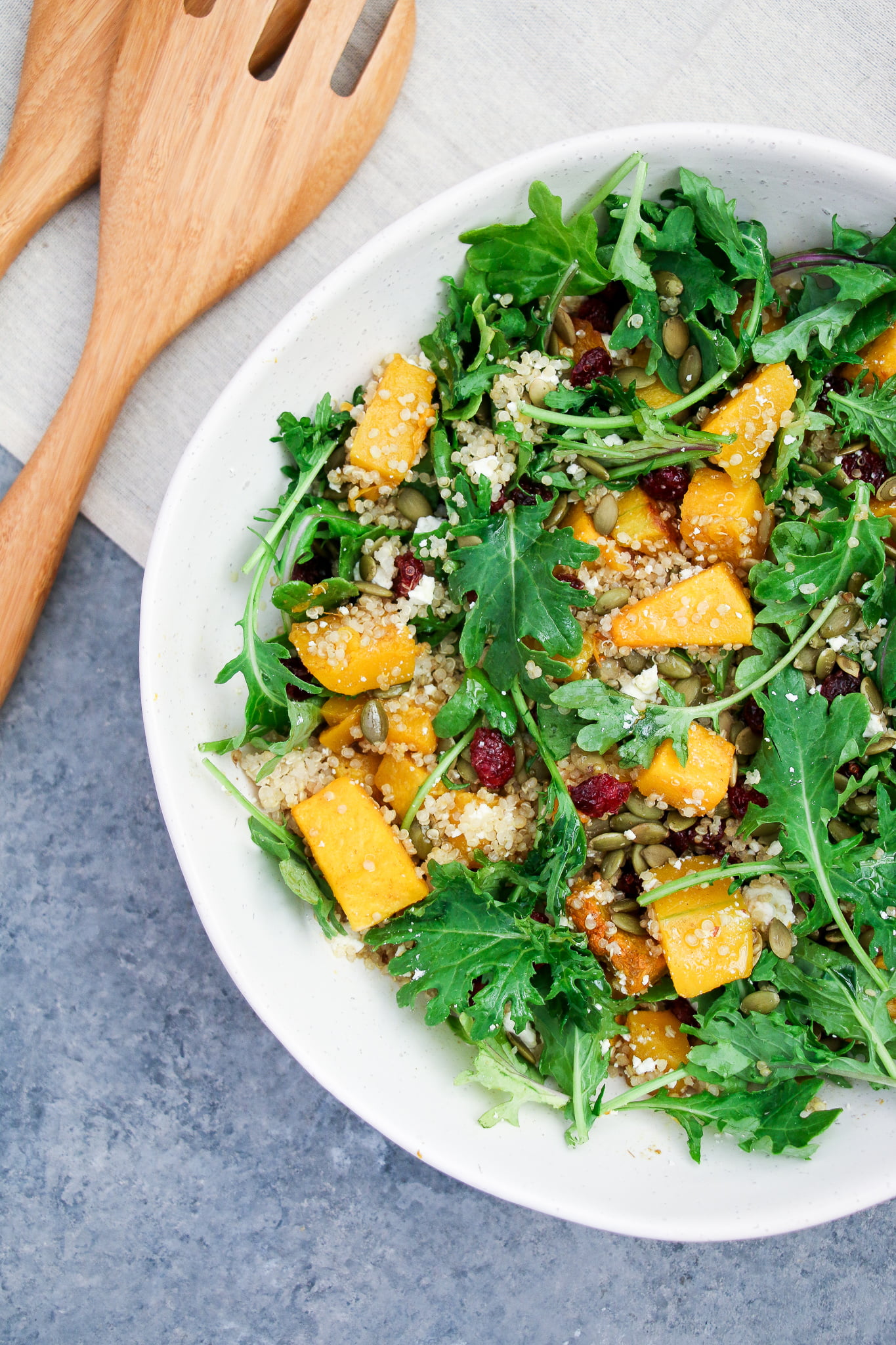 Pumpkin, cranberry and arugula quinoa salad in a white salad bowl on a gray background