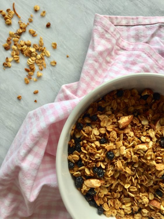 Vanilla, almond and coconut granola in a white bowl on a pink background.