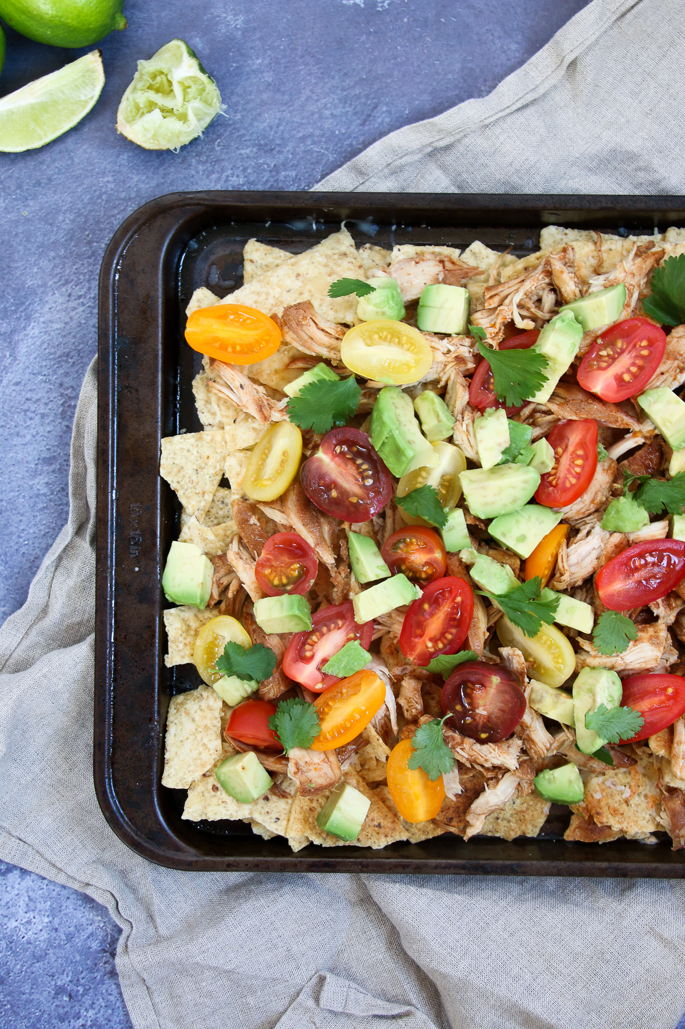 Close-up healthy chicken nachos on a black sheet pan on a blue background