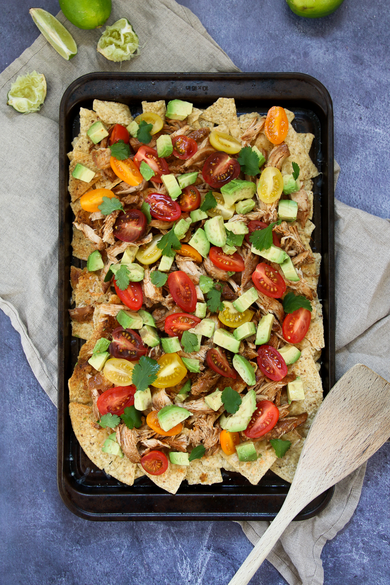 Healthy chicken nachos on a black sheet pan on a blue background
