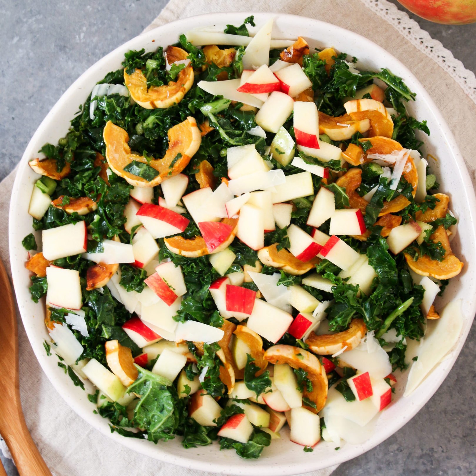 Raosted delicata squash and apple kale salad with honey mustard dressing in a white bowl on a gray background