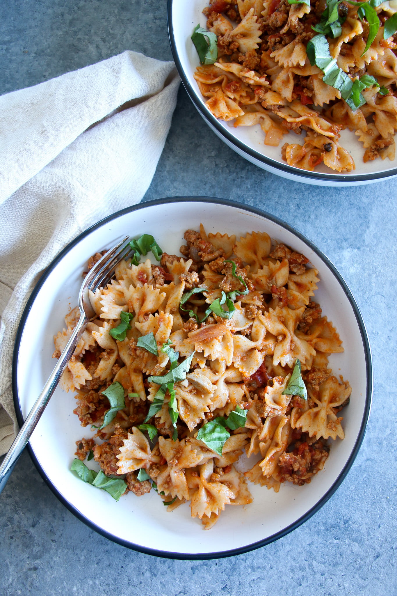 Creamy ground turkey pasta in white bowls with a beige towel on a gray background
