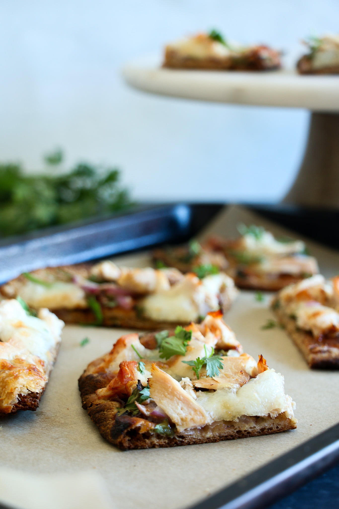 Barbecue chicken naan bread pizza slice on parchment paper on a baking tray with fresh cilantro in the background