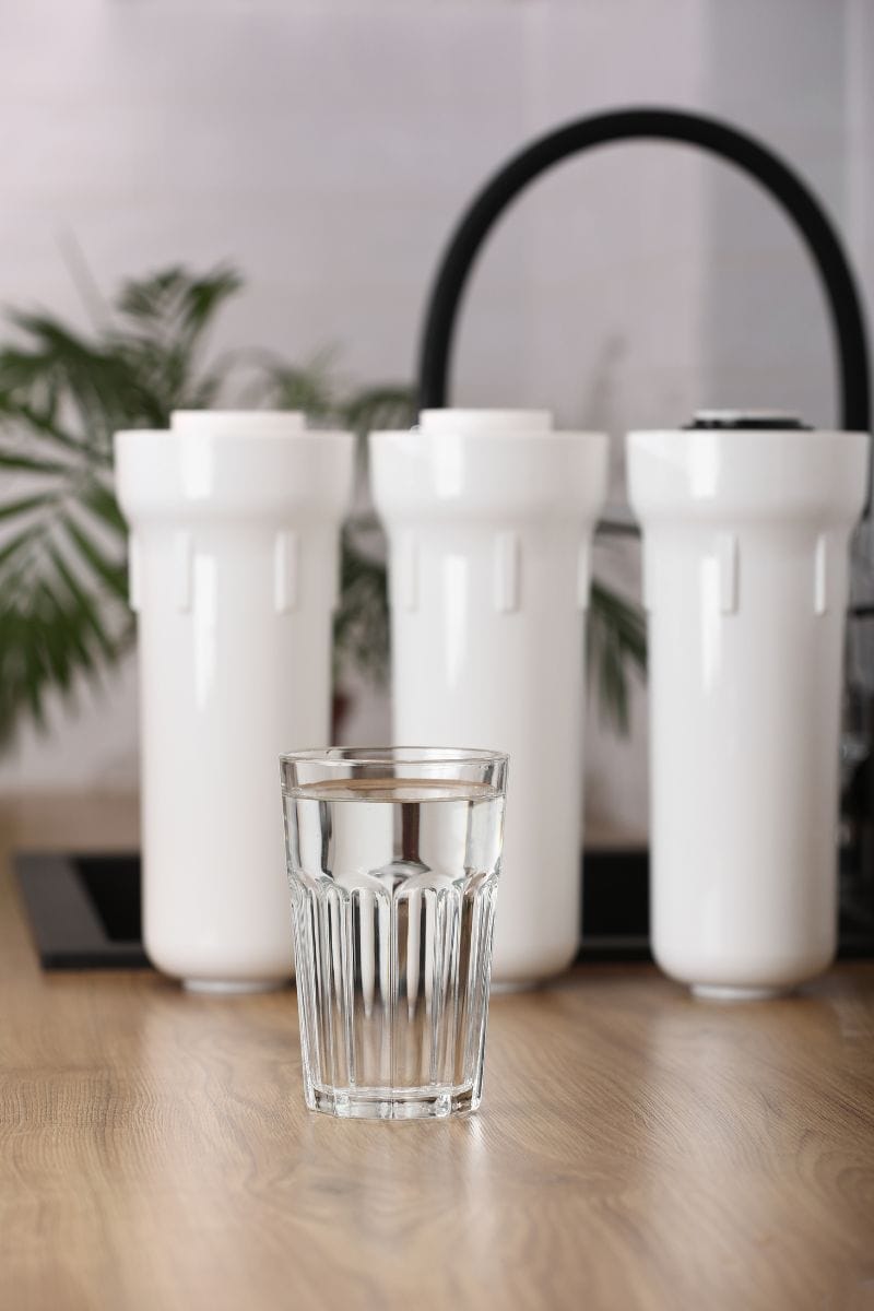 Glass of filtered water with filter in the background to remove PFAS.